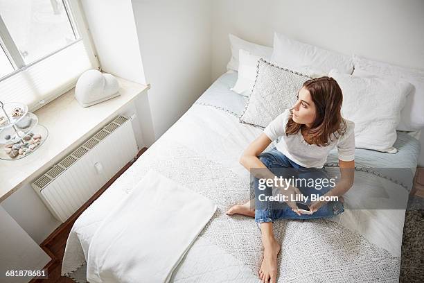 high level view of beautiful young woman sitting on bed gazing through window - bed top view stock-fotos und bilder
