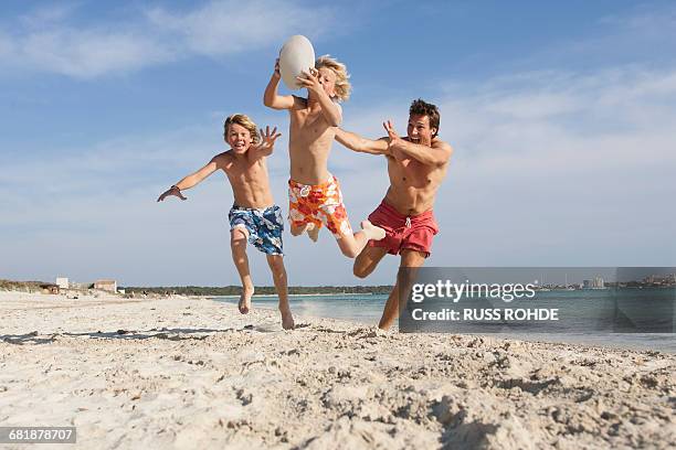 boy jumping with rugby ball chased by brother and father on beach, majorca, spain - preteen swimwear bildbanksfoton och bilder