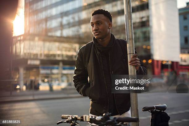thoughtful teenager standing by pole against buildings in city - boy thoughtful stock-fotos und bilder