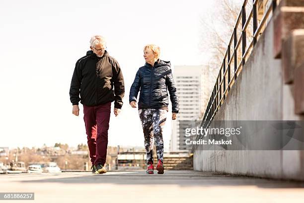senior couple in sportswear walking on sidewalk against clear sky - old shoes stockfoto's en -beelden