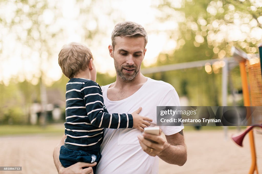 Father using phone while carrying son at playground