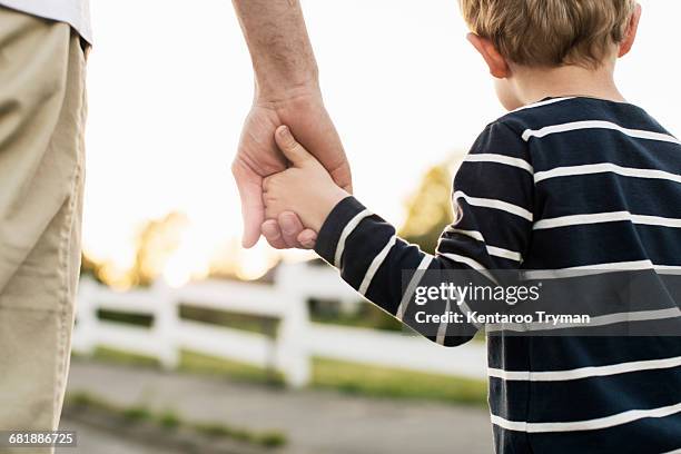 rear view of father and son holding hands while standing outdoors - hände halten stock-fotos und bilder