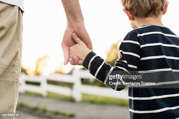 rear view of father and son holding hands while standing outdoors - holding hands foto e immagini stock