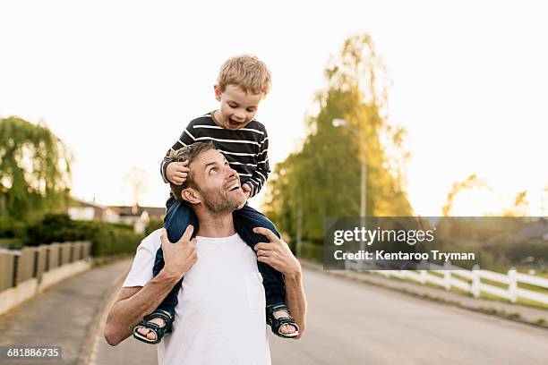 happy father carrying son on shoulders while standing at street against clear sky - llevar al hombro fotografías e imágenes de stock