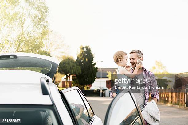 father carrying son with stuffed toy while standing by car on street - family front door stock-fotos und bilder