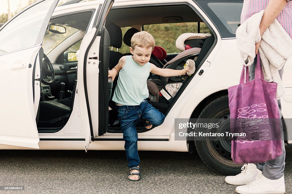 Boy disembarking from car while father standing with bag on street