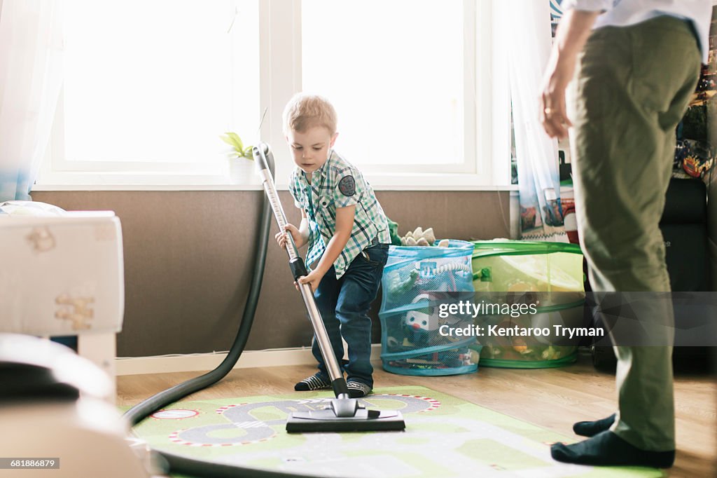 Boy vacuuming floor while father standing at home