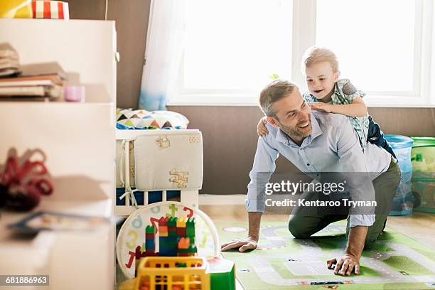 boy riding on fathers back while playing at home - crawling stock-fotos und bilder