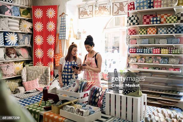 Female owners using smart phone and digital tablet while standing in fabric shop