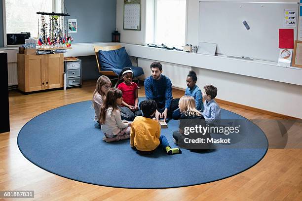 teacher playing with students while sitting on floor at school - montessori education stock-fotos und bilder