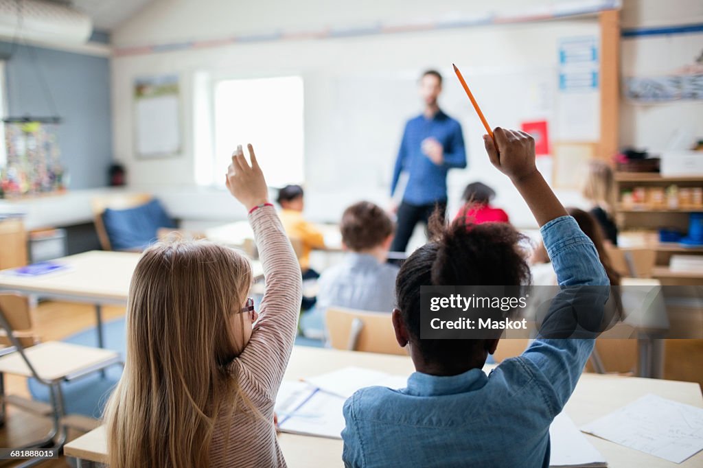 Rear view of students sitting with hands raised in classroom