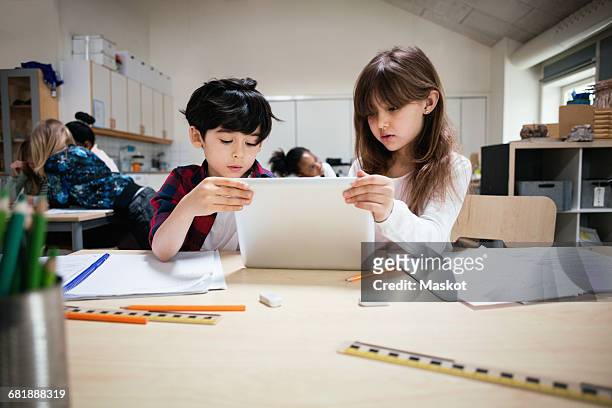 Concentrated students using digital tablet at desk in classroom