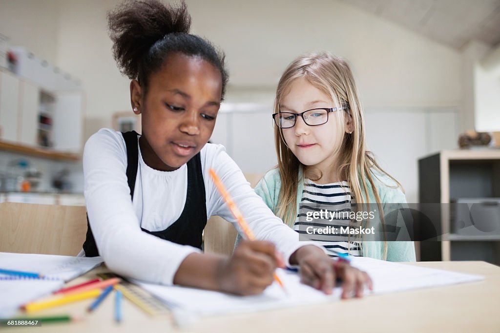 Girl assisting friend while studying in classroom at school