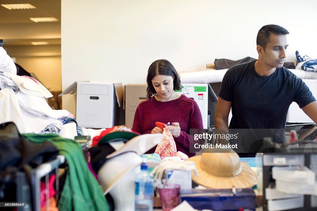 Serious woman holding tape dispenser while working with male volunteer at workshop