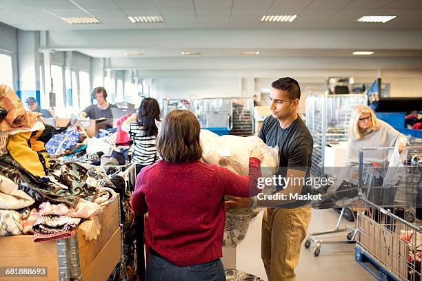 man assisting woman in holding plastic while volunteers working at workshop - fundraising stock-fotos und bilder