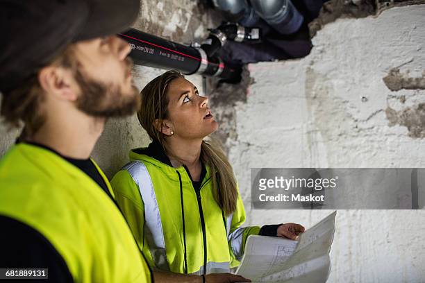 concentrated male and female plumbers looking up while reading document at basement - pipe women stock pictures, royalty-free photos & images