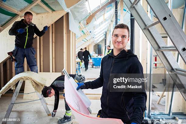 portrait of man holding blue prints while coworkers working in background - artisan portrait equipe photos et images de collection