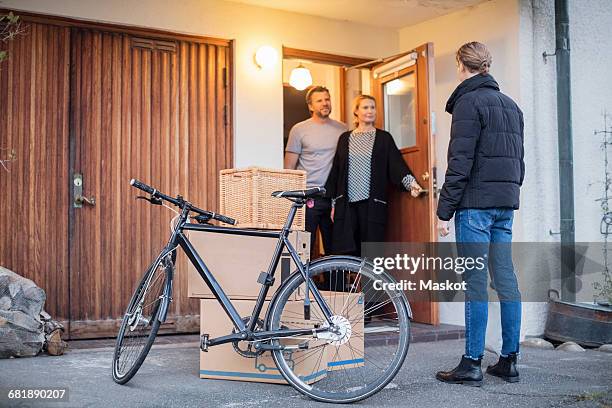 man looking at parents while standing with cardboard boxes and bicycle at house entrance - boomerang generation stock pictures, royalty-free photos & images