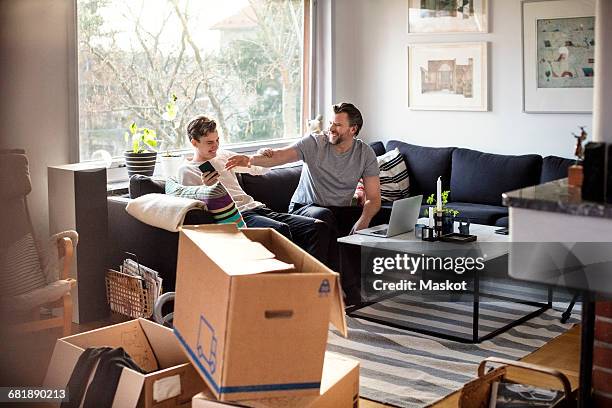 playful father and son sitting on sofa at new home - new home exterior stock pictures, royalty-free photos & images