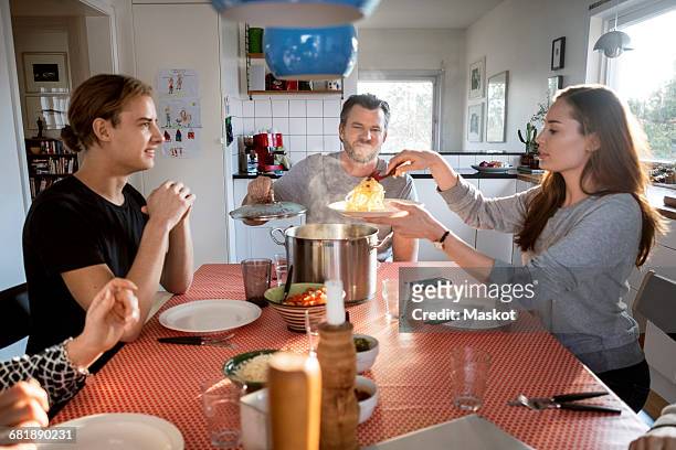 woman serving food in plate while sitting with family at dining table - seulement des adultes photos et images de collection