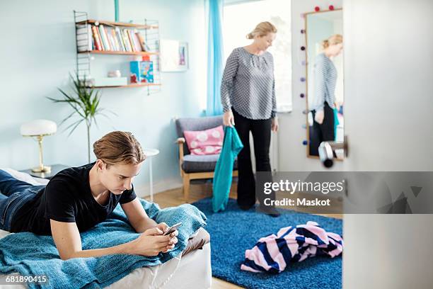 man using smart phone while lying on bed with mother holding clothes at new house - boomerang generation stock pictures, royalty-free photos & images