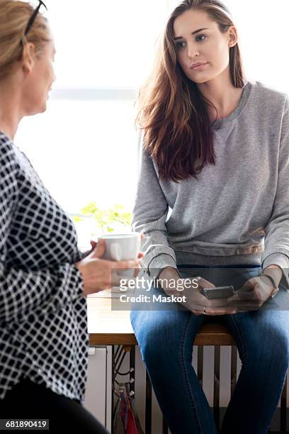 woman looking at mother while sitting on kitchen counter at new home - adults arguing stock pictures, royalty-free photos & images