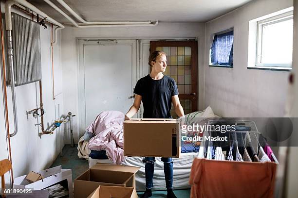full length of thoughtful man carrying cardboard box while sanding in bedroom - basement stock pictures, royalty-free photos & images
