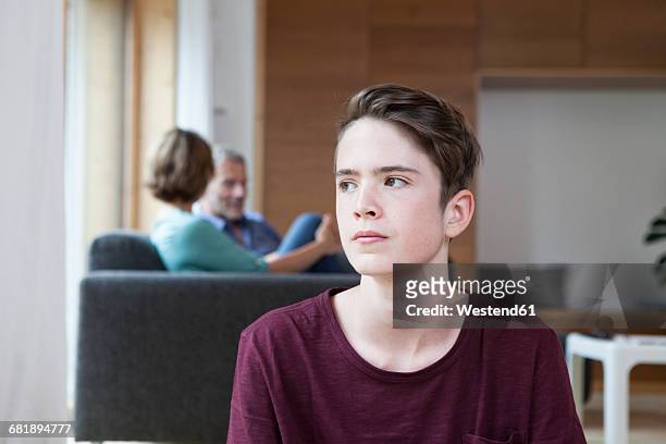 thoughtful teenage boy at home with parents in background - serious teenager boy stock pictures, royalty-free photos & images