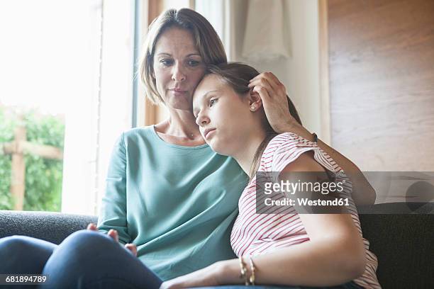 mother comforting daughter sitting on sofa - mourning stock-fotos und bilder