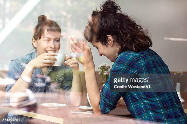 two laughing women sitting behind windowpane of a coffee shop - coffee shop chat imagens e fotografias de stock
