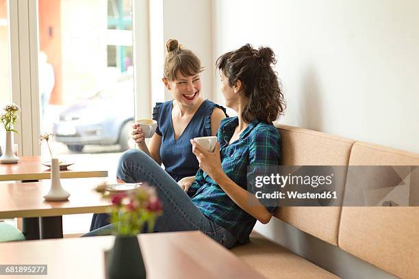 two happy friends in a coffee shop - knees together - fotografias e filmes do acervo