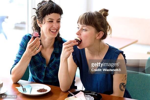 two friends sitting side by side in a coffee shop eating cup cakes - kuchen stock-fotos und bilder