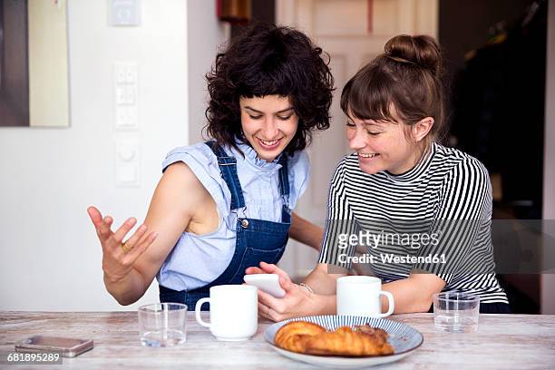 two women at breakfast table looking together at smartphone - women drinking coffee photos et images de collection