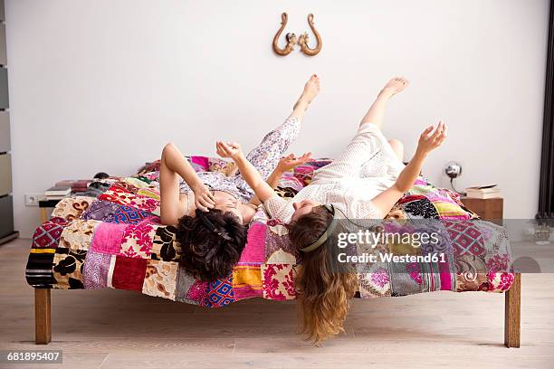 two best friends lying on bed with legs in the air listening music with headphones - patchwork stock-fotos und bilder