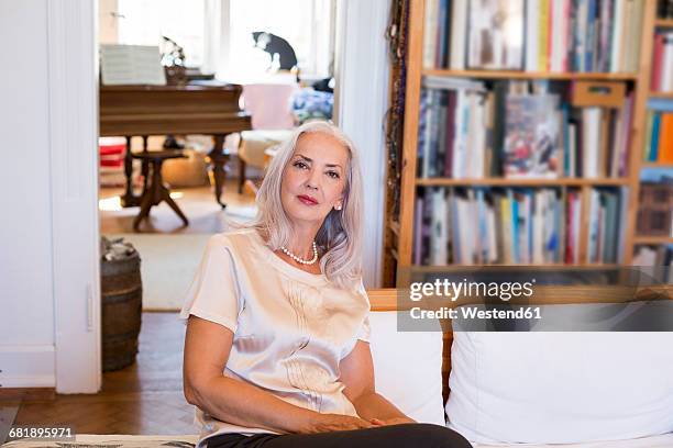 portrait of mature woman sitting on couch at home - une seule femme d'âge mûr photos et images de collection