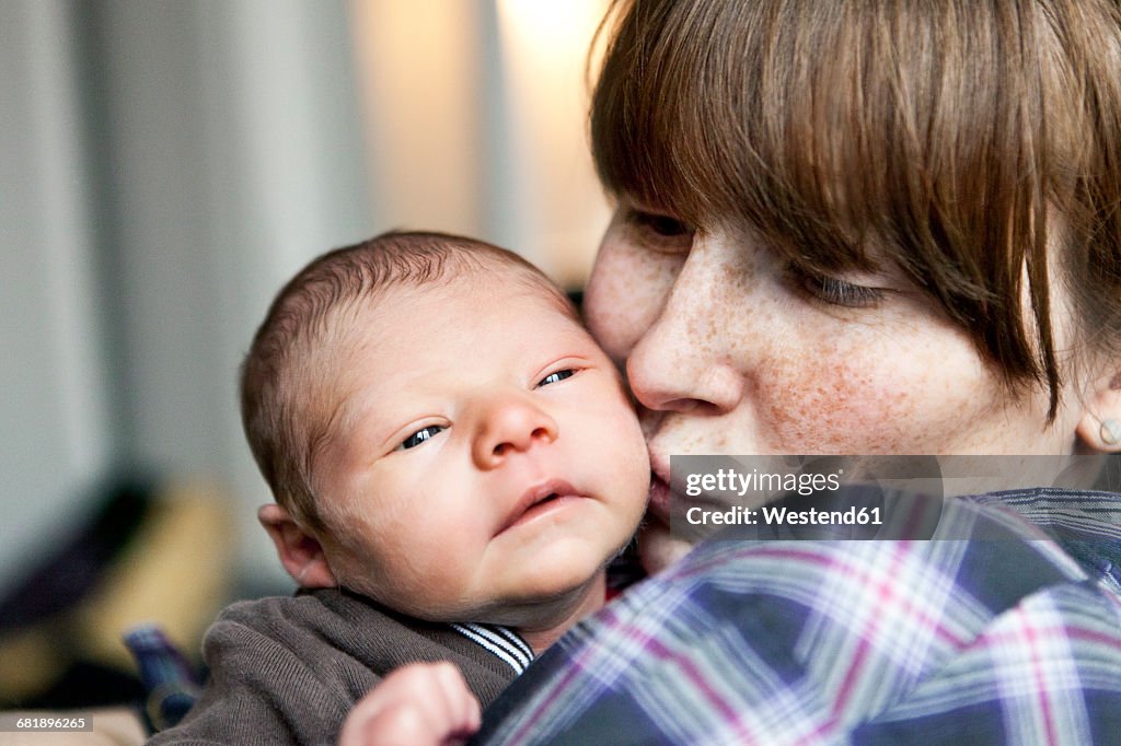 Freckled mother kissing her newborn baby son on the cheek