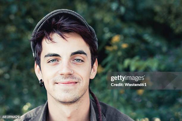 portrait of smiling young man with nose piercing and earring wearing cap - nose piercing - fotografias e filmes do acervo