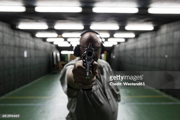 man aiming with a revolver in an indoor shooting range - tiro ao alvo imagens e fotografias de stock