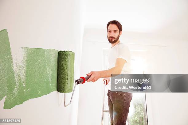 young man painting a wall green - painting activity stock-fotos und bilder