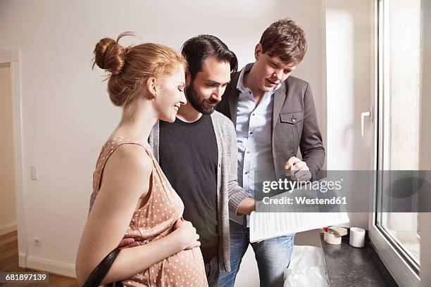 real estate agent showing expecting parents a contract in a new apartment - real couple stock-fotos und bilder