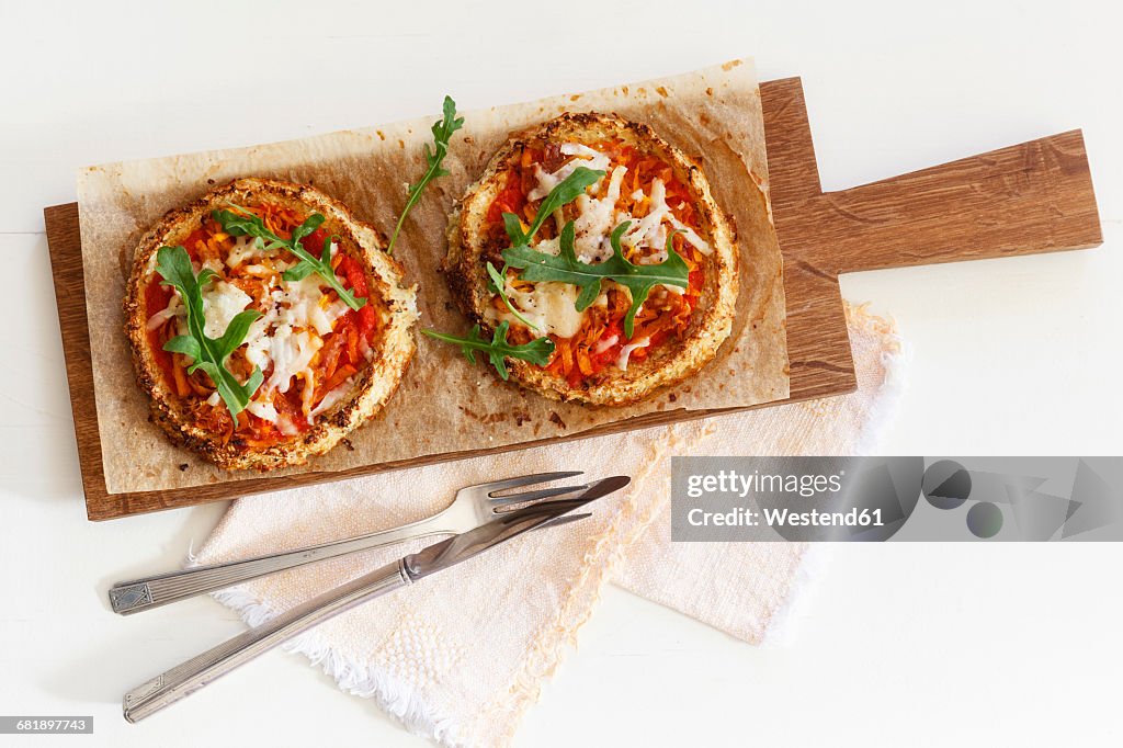 Two homemade glutenfree mini pizzas with cauliflower, pumpkin and rocket on wooden board