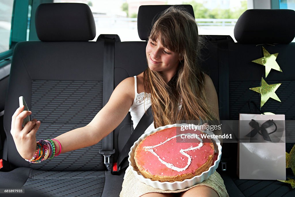 Girl taking a selfie in car with heart-shaped cake