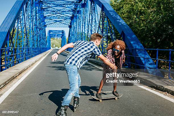 happy young couple with inline skates and skateboard on a bridge - inline skating - fotografias e filmes do acervo
