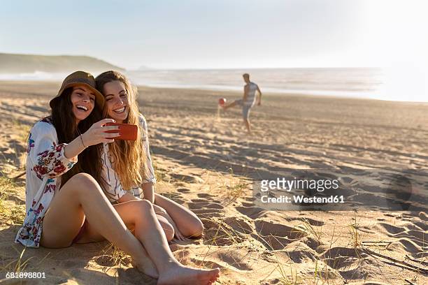 two best friends sitting on the beach taking selfie with smartphone - beach girl ストックフォトと画像