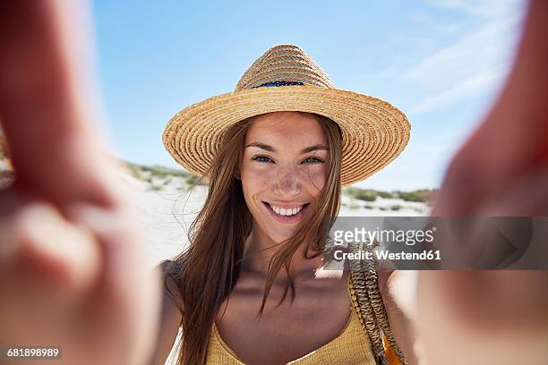portrait of smiling young woman on the beach - weißer hut stock-fotos und bilder