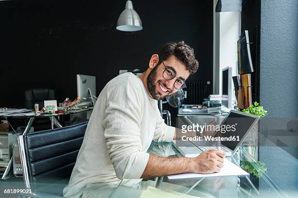 portrait of smiling young man working with laptop at desk in a modern office - solo un uomo giovane foto e immagini stock