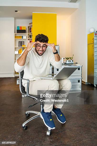 young man with laptop in a modern office pulling funny faces - bürostuhl stock-fotos und bilder
