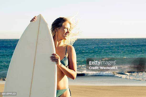 spain, tenerife, young blonde surfer on the beach - beach hold surfboard stock-fotos und bilder