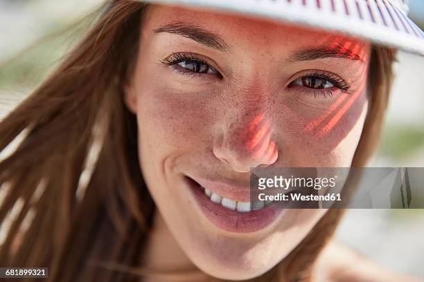 portrait of smiling young woman wearing sun visor - sun on face stock-fotos und bilder