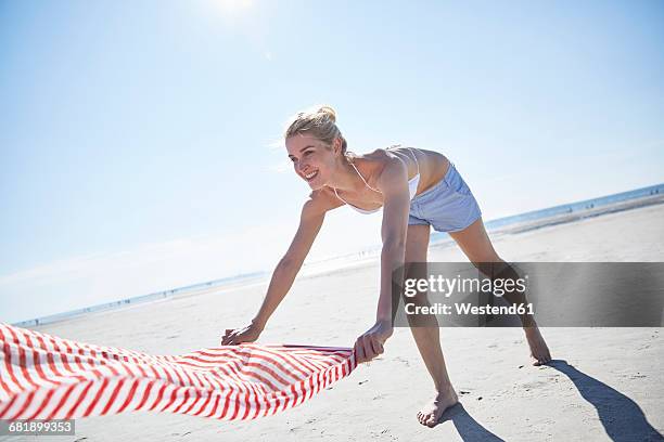 young woman spreading out towel on the beach - região marítima do norte da alemanha imagens e fotografias de stock